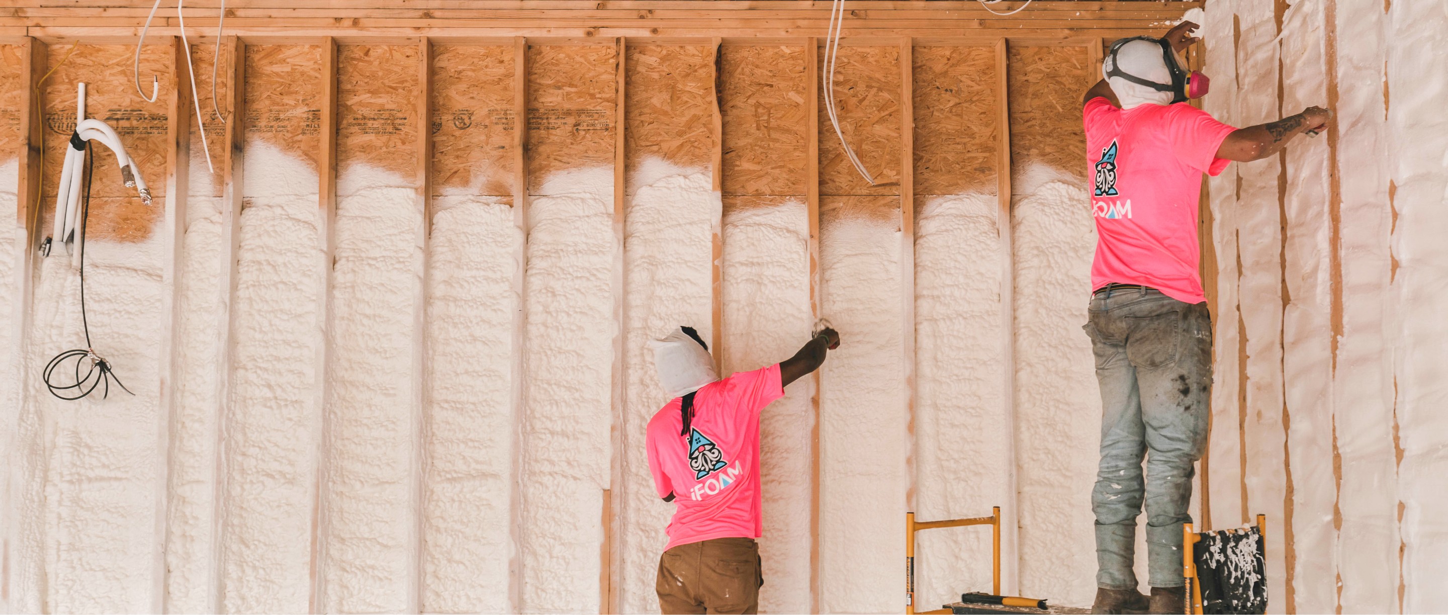 Two iFOAM technicians spray foam on walls