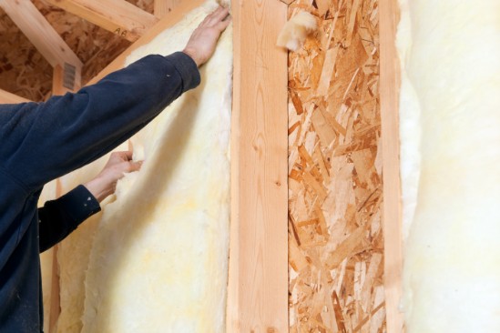 A person installing rolls of yellow BATT insulation in a new home