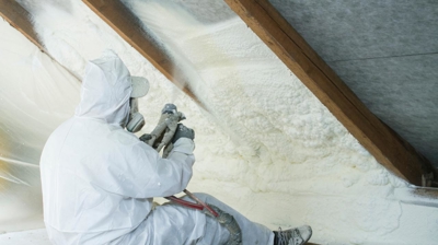 Technician spraying spray foam insulation on the side of an attic